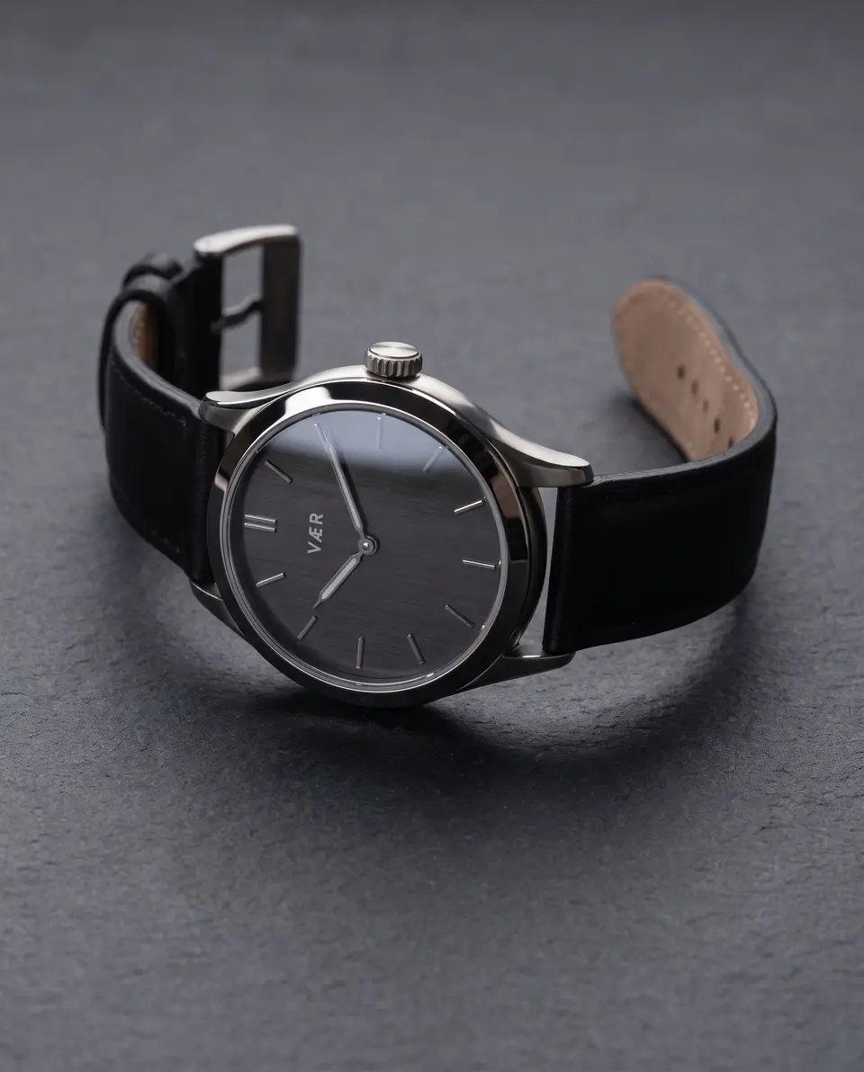 VÆR / 01 lying on dark stone, strap open, titanium case catching a line of light.